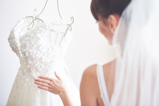 La novia elegante pone un vestido de novia en su habitación.