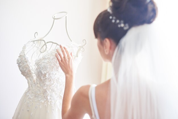 La novia elegante pone un vestido de novia en su habitación.