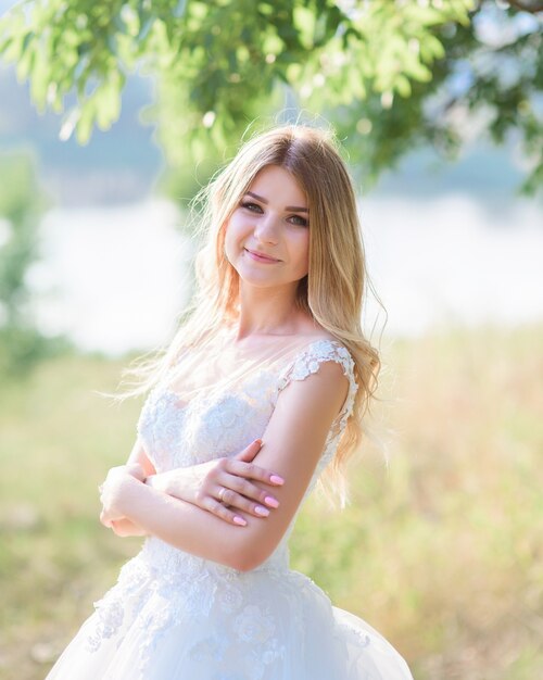 Novia encantadora se ve feliz posando en su hermoso vestido afuera en un día soleado de verano