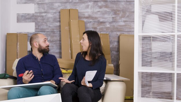 Novia golpeando a su novio con instrucciones mientras ensambla muebles en su nuevo apartamento.