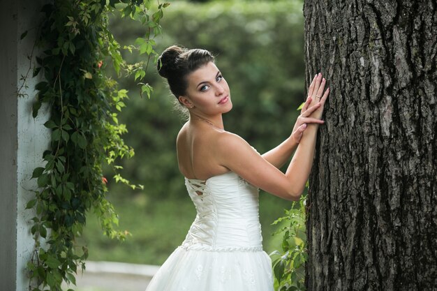 Novia guapa posando con la mano en un tronco