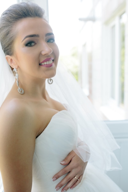 Novia hermosa joven posando contra la ventana en la habitación del hotel