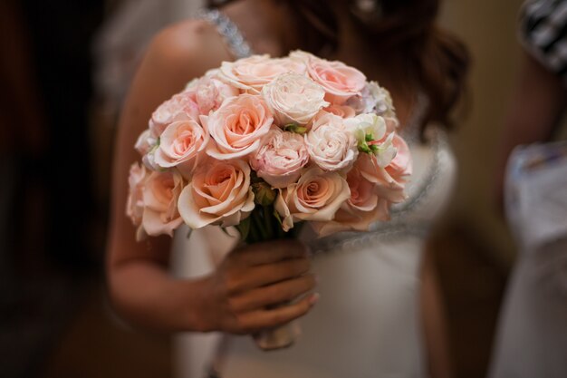 Novia hermosa que sostiene el primer del ramo de las rosas rosadas