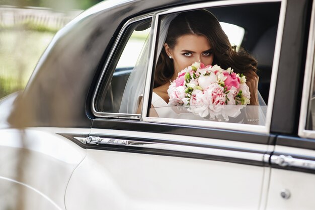 Foto gratuita la novia hermosa se sienta con el ramo de la boda en un coche retro y se divierte