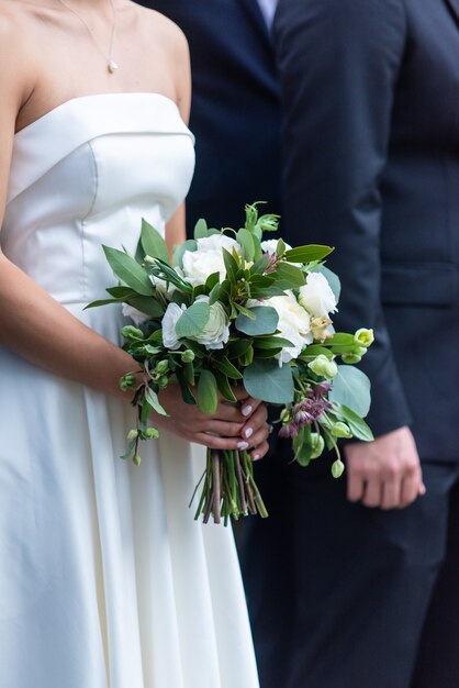 Una novia en un hermoso vestido de novia blanco con un ramo de novia de pie junto al novio