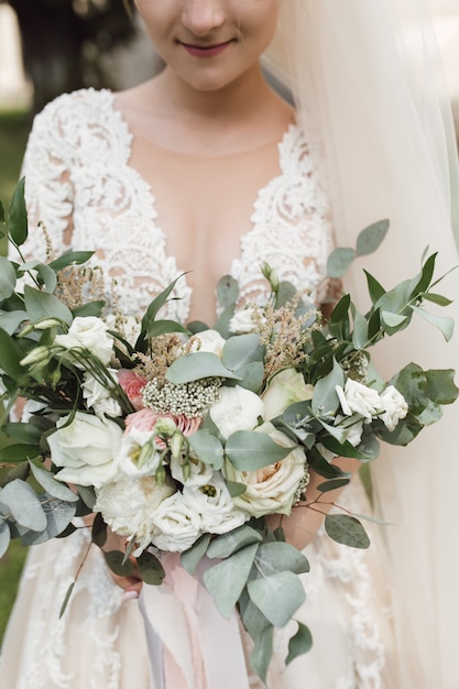 La novia en el hermoso vestido tiene un ramo de novia con eucalipto y rosas blancas.