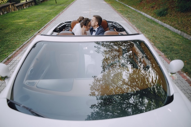 Una novia joven y hermosa está sentada en un coche con su marido