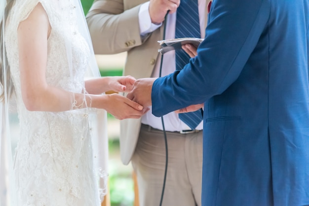 Novia con un lujoso vestido blanco y un novio con un traje azul durante la ceremonia de la boda con el sacerdote