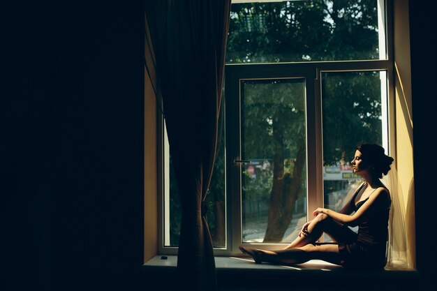 Novia por la mañana sentada en el alféizar de la ventana