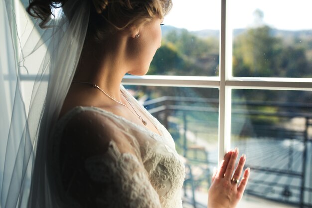 Novia mirando por la ventana desde la habitación del hotel