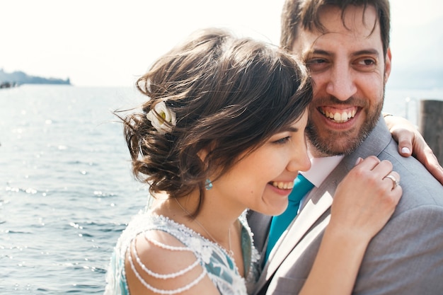 La novia y el novio se abrazan tiernamente sentado en la playa sobre el agua