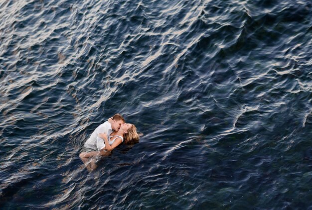 Novia y novio abrazándose en el agua del océano y besándose
