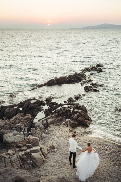 La novia y el novio caminan hacia la puesta de sol sobre el mar