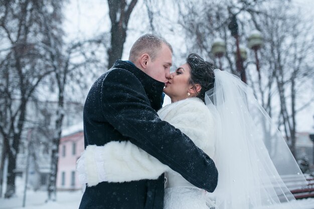 La novia y el novio caminando por la ciudad europea en la nieve.