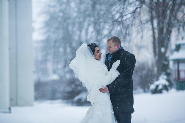 La novia y el novio caminando por la ciudad europea en la nieve.