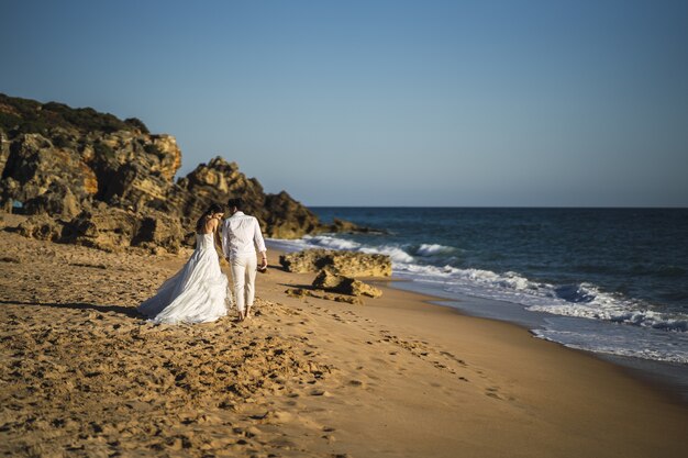 La novia y el novio caminando en la playa de arena