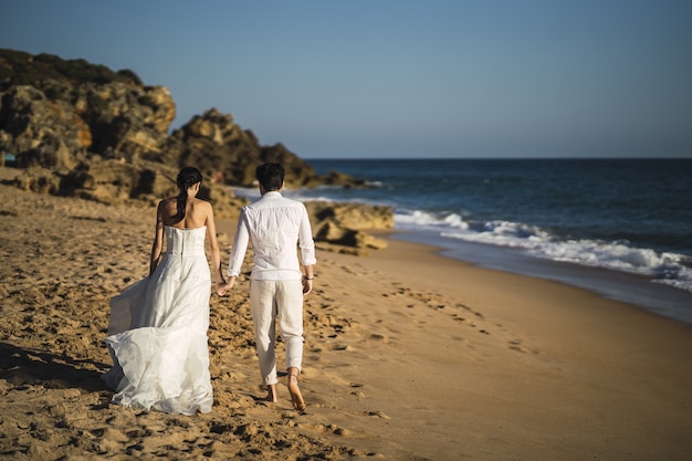 La novia y el novio caminando en la playa de arena