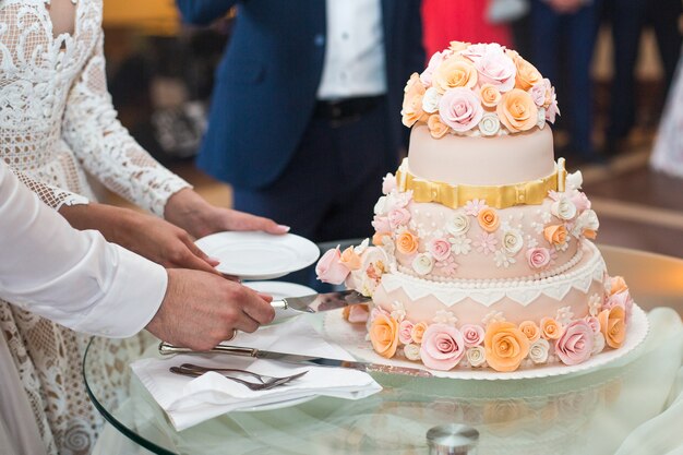 Novia y el novio cortan delicioso pastel de bodas decorado con beige