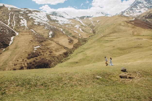 la novia y el novio están caminando sobre la hierba en verano en las altas montañas