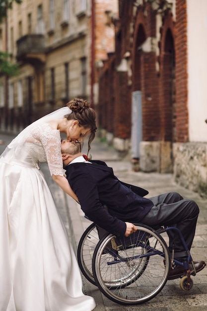 Novia y el novio en la silla de ruedas posan en la antigua calle europea