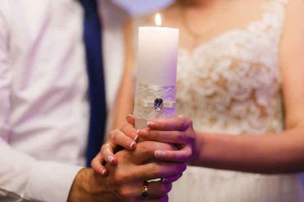 Novia y el novio sosteniendo la vela. Primer plano de las manos