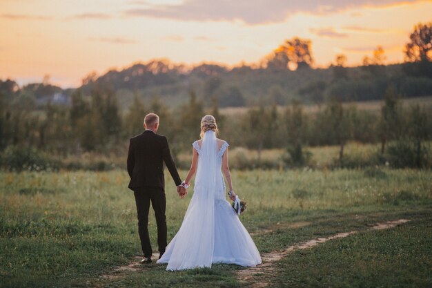 La novia y el novio tomados de la mano después de la ceremonia de la boda en un campo al atardecer