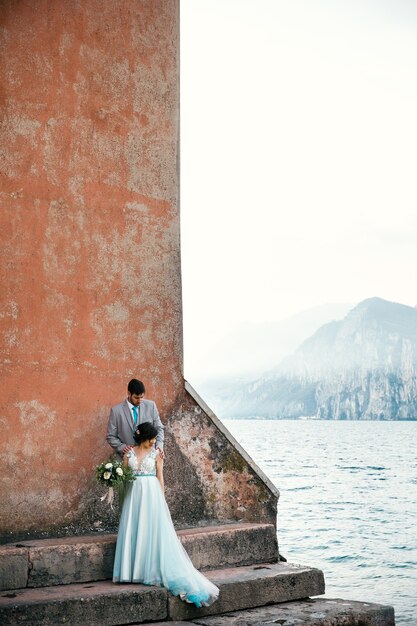 La novia y el novio se unen en la orilla antes del mar