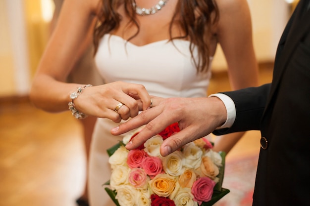 La novia pone el anillo en el dedo del novio sobre el ramo de boda brillante