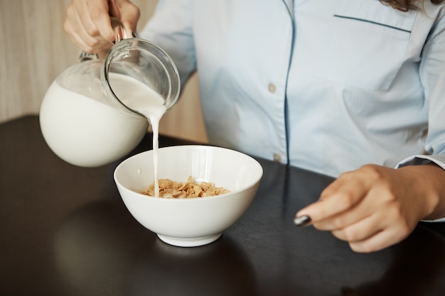 Novia preparando desayuno sencillo en la mañana. Captura recortada de mujer en ropa de dormir vertiendo leche en un tazón con cereales, con ganas de comer rápido y vestirse para ir a la oficina