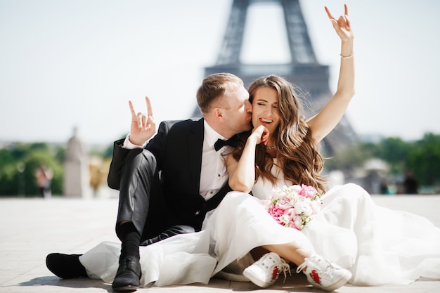 La novia se sienta en snickers ante la torre Eiffel en París mientras el novio la besa