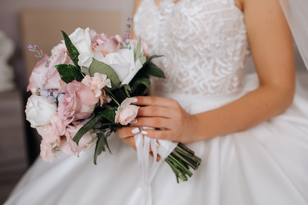 La novia sostiene el hermoso ramo de novia con rosas blancas y rosas