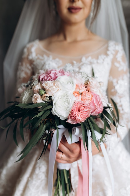 La novia sostiene el hermoso ramo de novia con rosas blancas y rosas