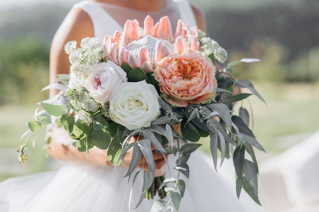 La novia sostiene el hermoso ramo de novia con rosas, eucaliptos y protea gigante