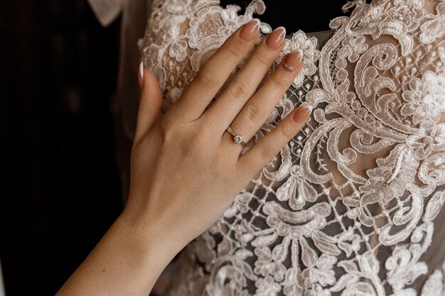 La novia sostiene su mano en el vestido de novia colgado