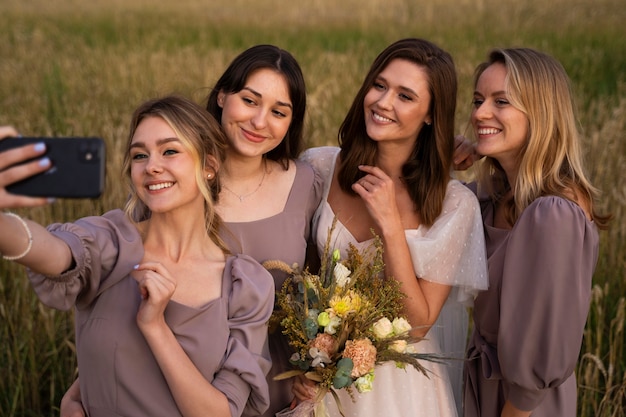 Novia de tiro medio y damas de honor tomando selfie