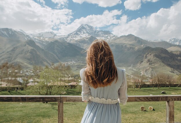 novia en un vestido esperando al novio mirando a las montañas con picos de nieve