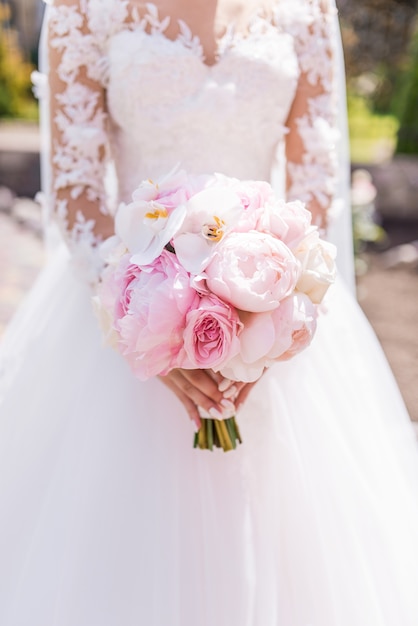 La novia en vestido rico tiene ramo rosado de la boda de orquídeas y peonías