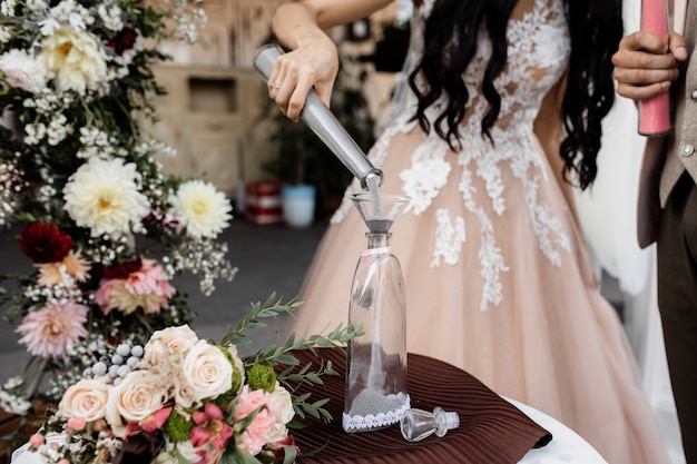 La novia vierte arena gris en una botella