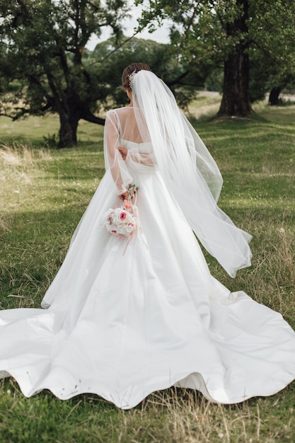 Novias se para en un parque y sostiene un ramo de novia a la espalda, sin rostro