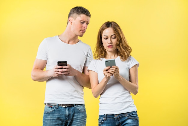 Novio ansioso espiando a su novia enviando mensajes de texto en un teléfono móvil con fondo amarillo