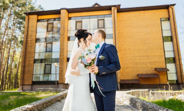 El novio besa a la novia en la frente después de la ceremonia de boda contra una casa de madera grande