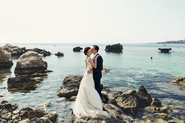 Novio besos novia oferta en las rocas sobre el océano