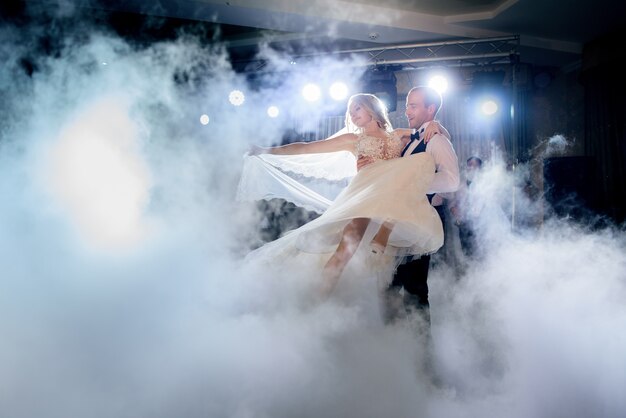 El novio da vuelta a la novia en el humo que baila por primera vez