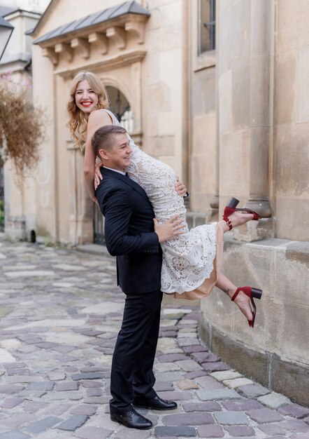 El novio lleva a la novia en el hombro, feliz pareja, día de la boda, al aire libre