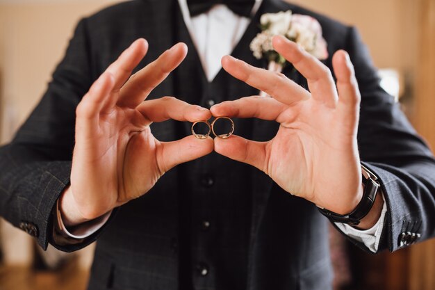 Novio muestra dos anillos de boda, sin rostro.