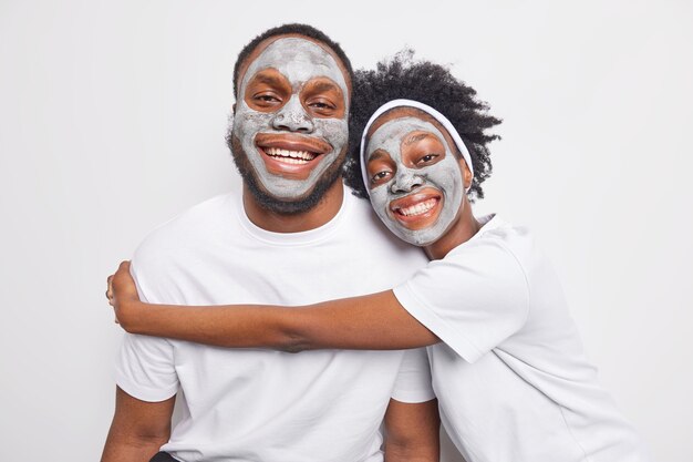 Novio y novia afroamericanos jóvenes abrazan con amor tienen buenas relaciones aplicar máscaras de arcilla en la cara para rejuvenecer la piel sonrisa alegremente aislada sobre pared blanca