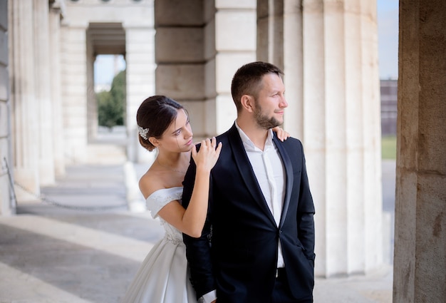 Novio y novia está de pie cerca de la enorme columna en el cálido día soleado