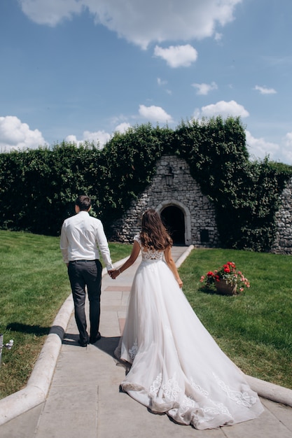 El novio y la novia están tomados de la mano y caminan hacia una puerta en un muro de piedra en el día soleado