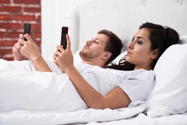 Novio y novia de lado mirando su teléfono después de despertarse