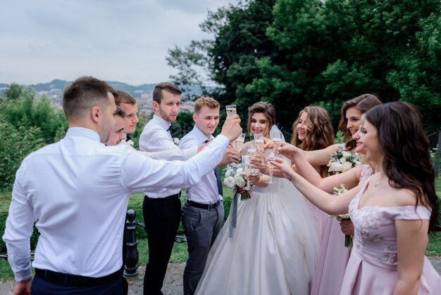 El novio, la novia, los mejores hombres y las damas de honor beben champán al aire libre el día de la boda.